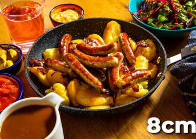 A pan full of Nürnberger Bratwurst on roast potatoes